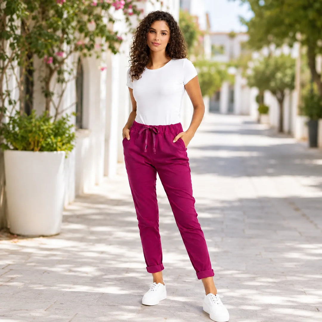 Woman wearing magenta magic pants with white top and trainers in an outdoor lifestyle fashion setting