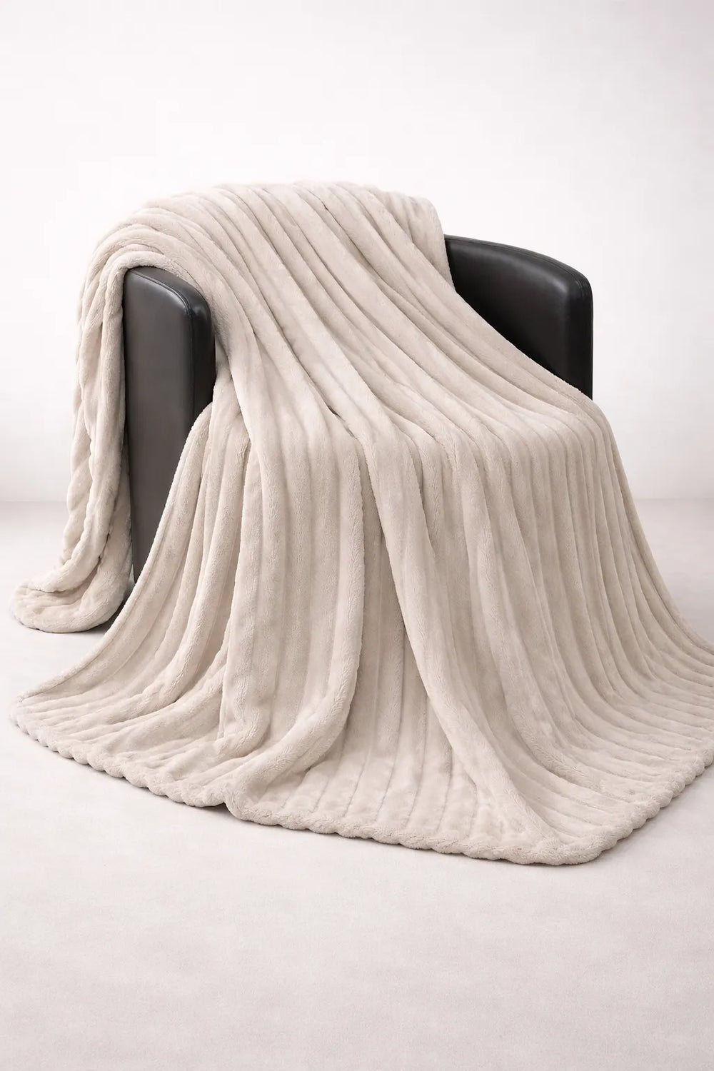 Beige knitted blanket draped over a black chair on a white background