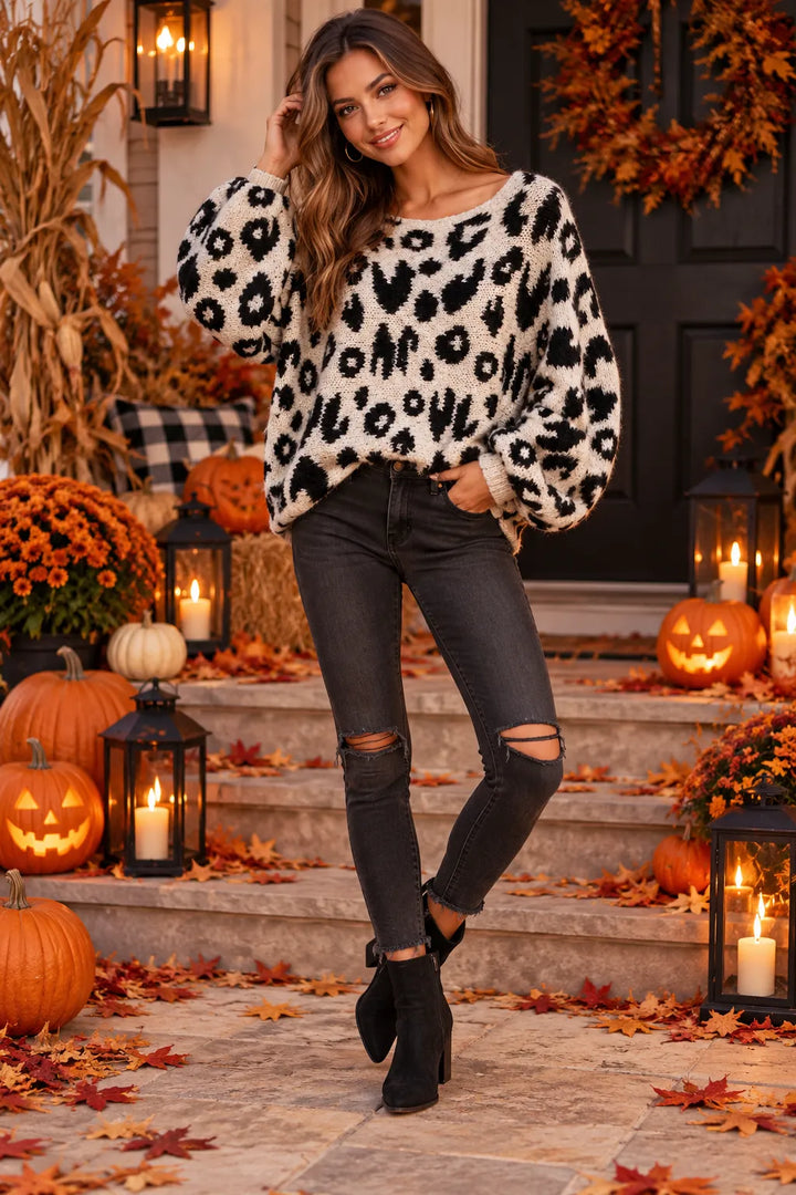 A woman stands on outdoor steps decorated for Halloween, wearing a fuzzy off-white knit sweater with a black leopard print pattern, black distressed skinny jeans, and black ankle boots.