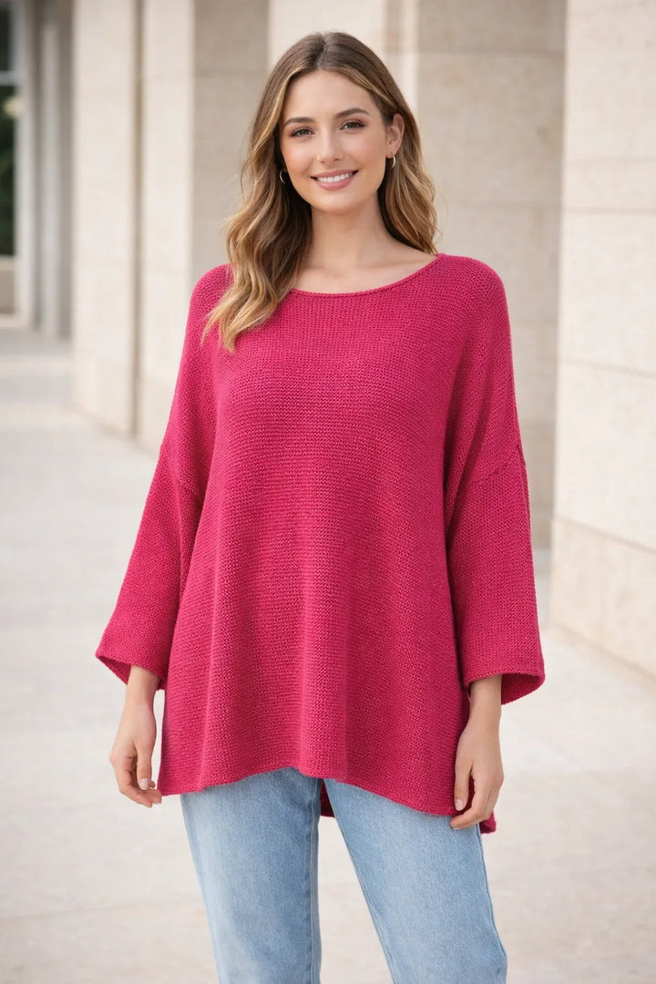 Woman wearing a pink sweater and light blue jeans standing outdoors.