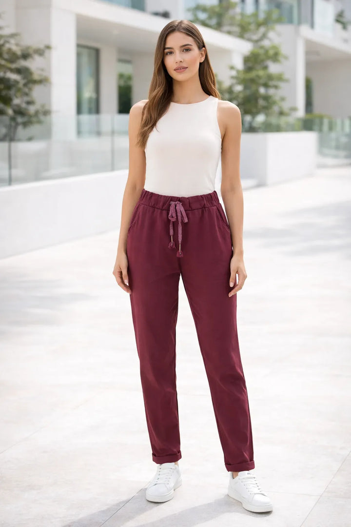 Woman wearing a white sleeveless top and burgundy pants standing on a modern architectural background.