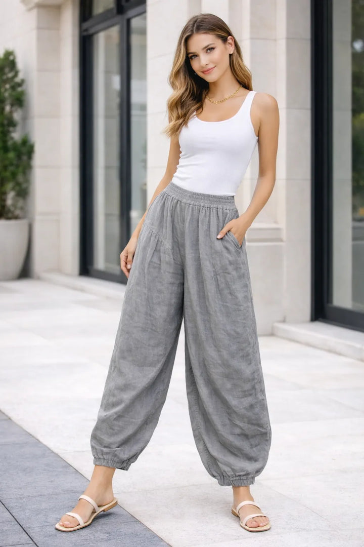 Woman wearing a white tank top and Light gray wide-leg pants standing outside a building.