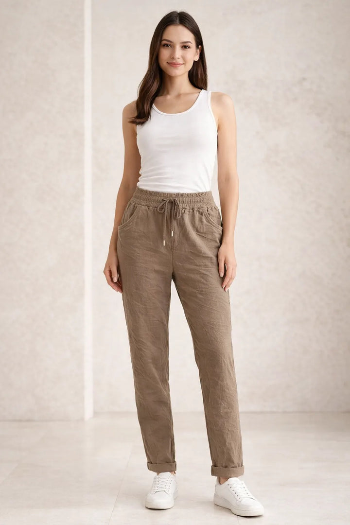 Woman wearing a white tank top and Mocha pants against a plain background