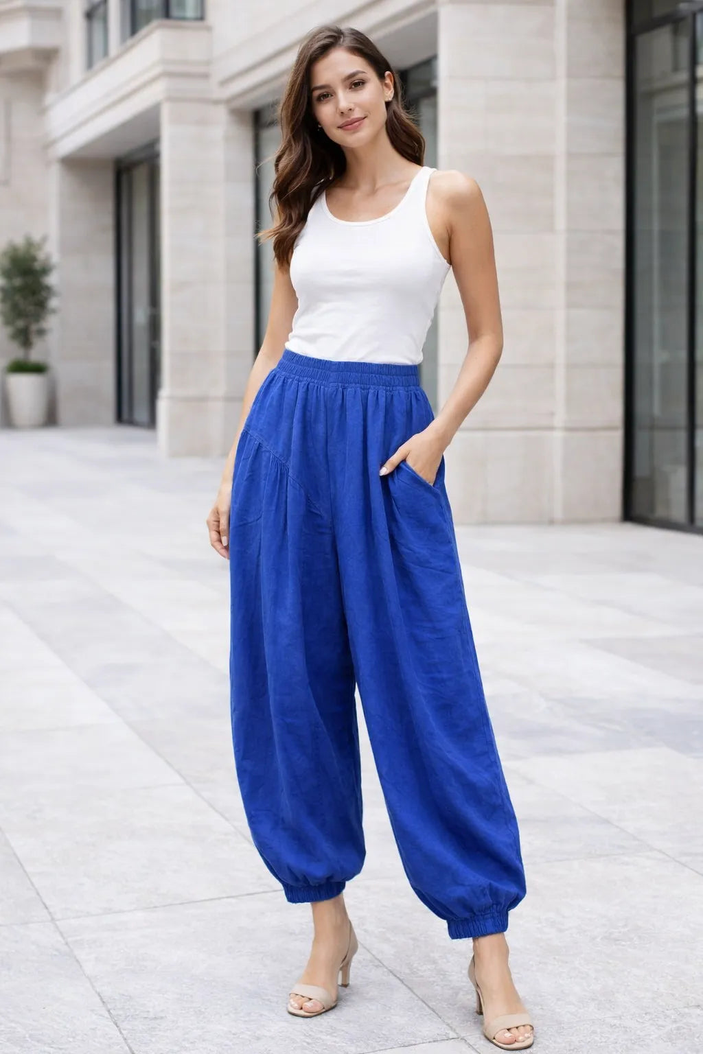 Woman wearing a white tank top and Royal blue high-waisted pants standing on a city street.