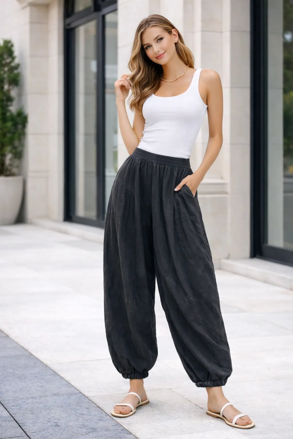 Woman wearing a white tank top and black high-waisted pants standing on a sidewalk.
