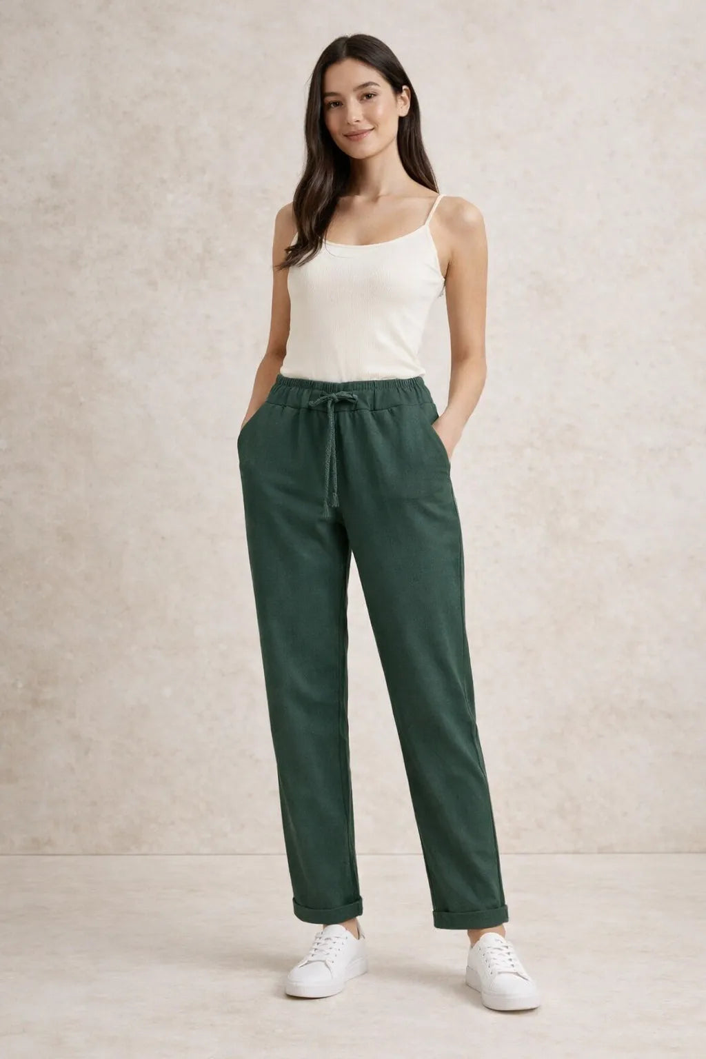 Woman wearing a white tank top and green pants against a beige background