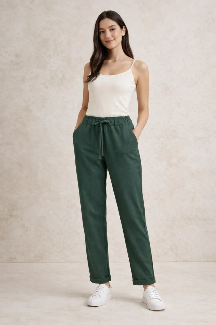 Woman wearing a white tank top and green pants against a beige background