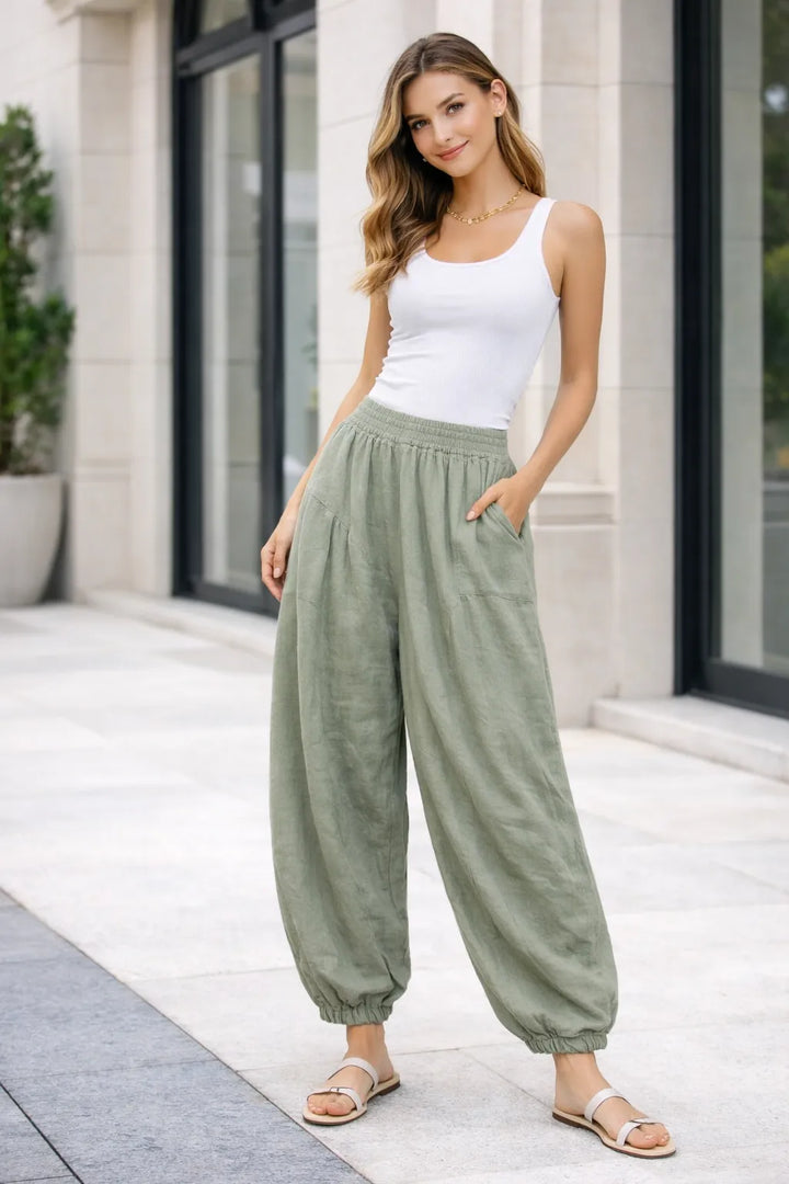 Woman wearing a white tank top and khaki high-waisted pants standing outdoors.