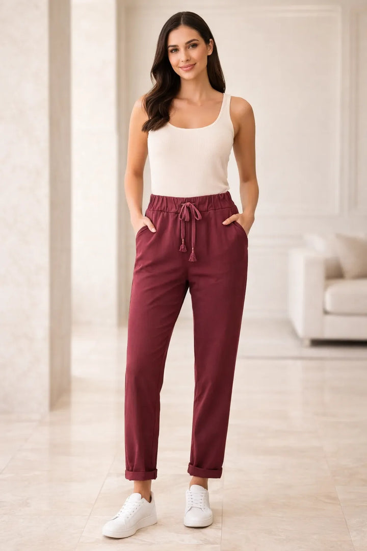 Woman wearing a white tank top and maroon pants in a bright room.