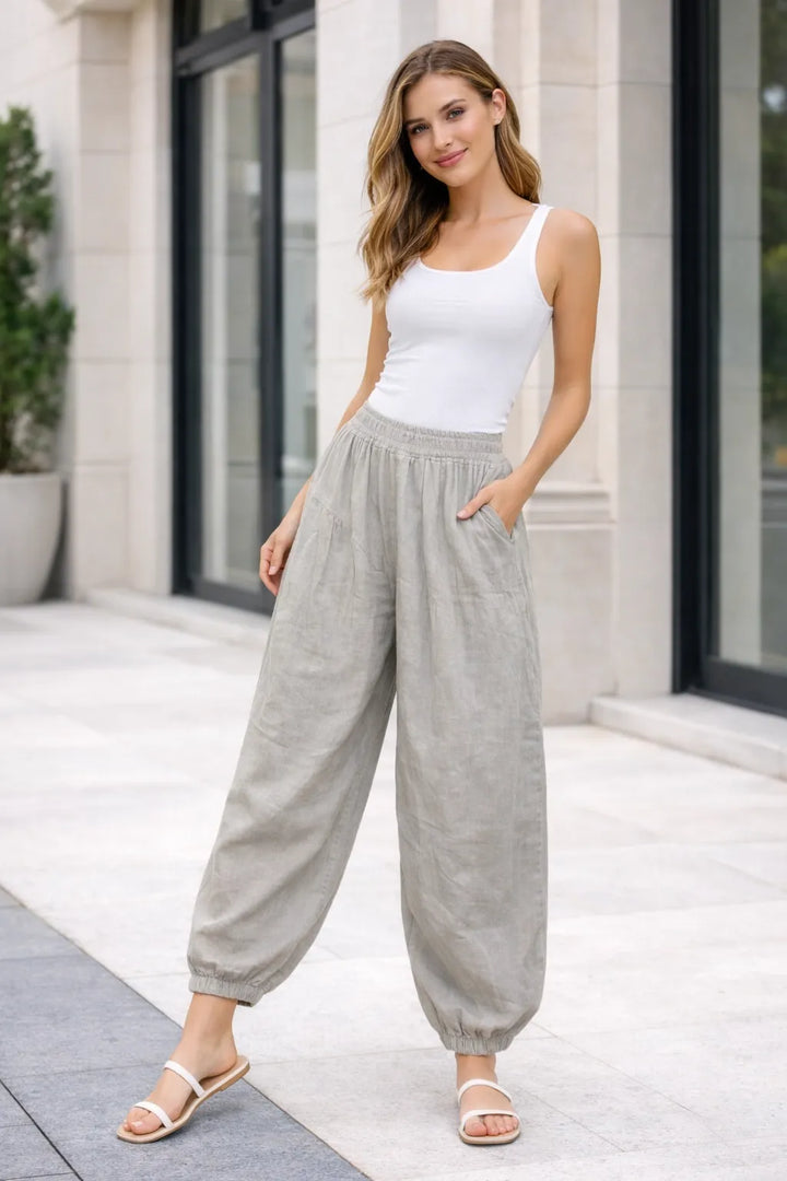 Woman wearing a white tank top and mocha high-waisted pants standing outdoors.