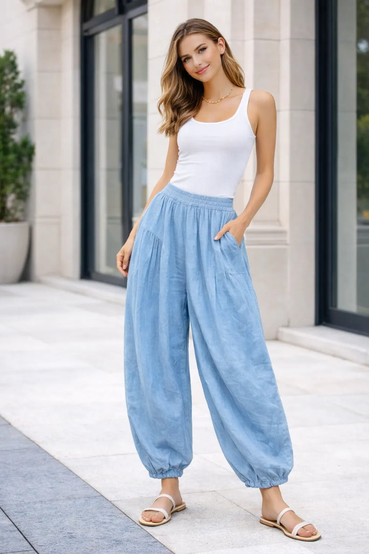Woman wearing a white top and light sky blue pants standing on a patio.