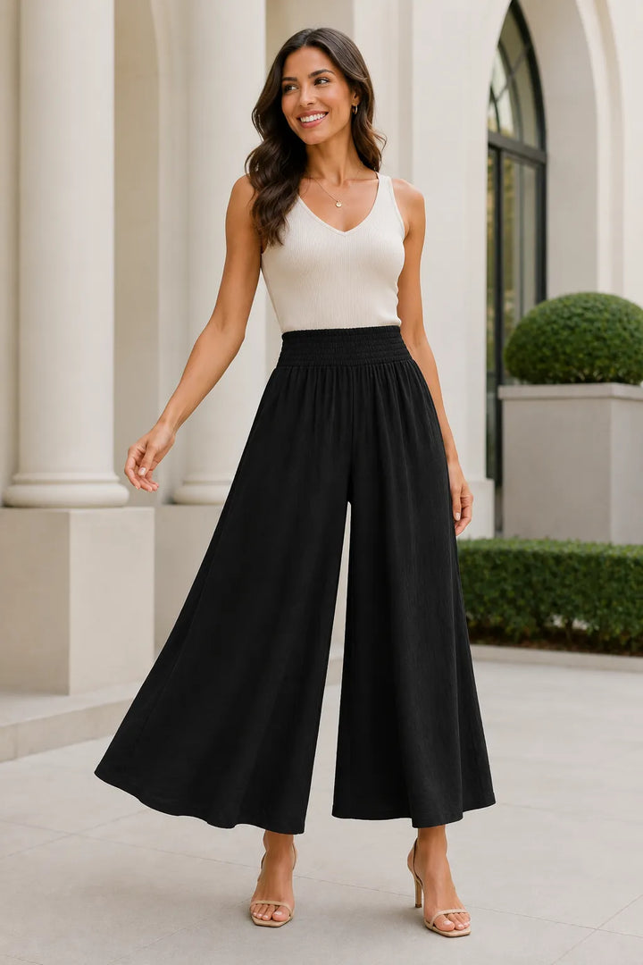 Woman wearing a white top and black wide-leg pants standing outdoors.