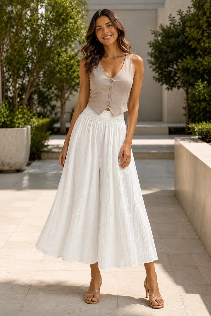 Woman in a light pink sleeveless top and white skirt standing outdoors.