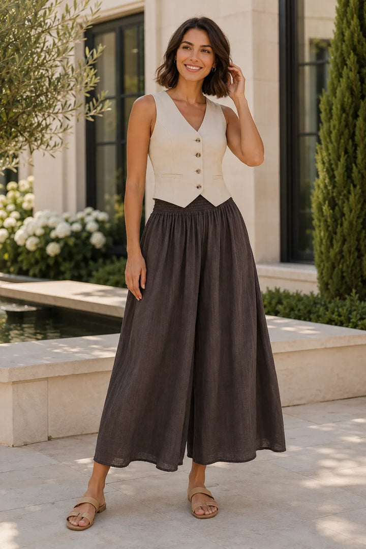 Woman wearing a sleeveless beige top with buttons and a long brown skirt outdoors.