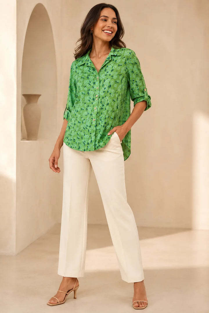 Woman wearing a green patterned blouse and white pants in a neutral setting