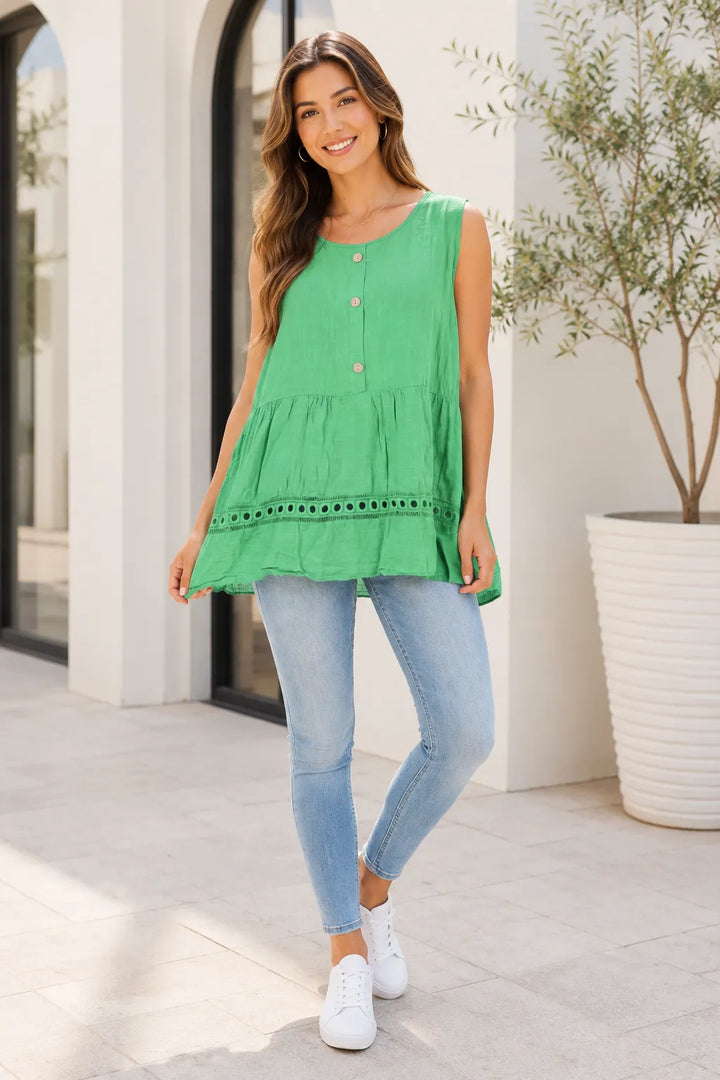 Woman wearing a green sleeveless top and light blue jeans standing outdoors.
