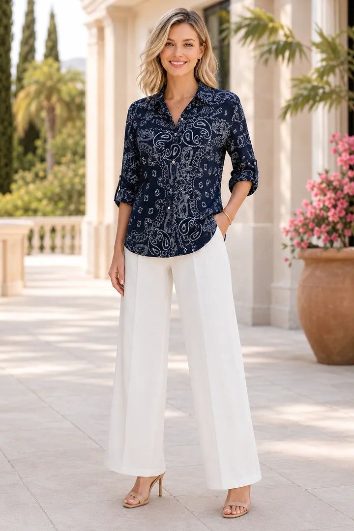 Woman wearing a navy patterned shirt and white pants standing outdoors.