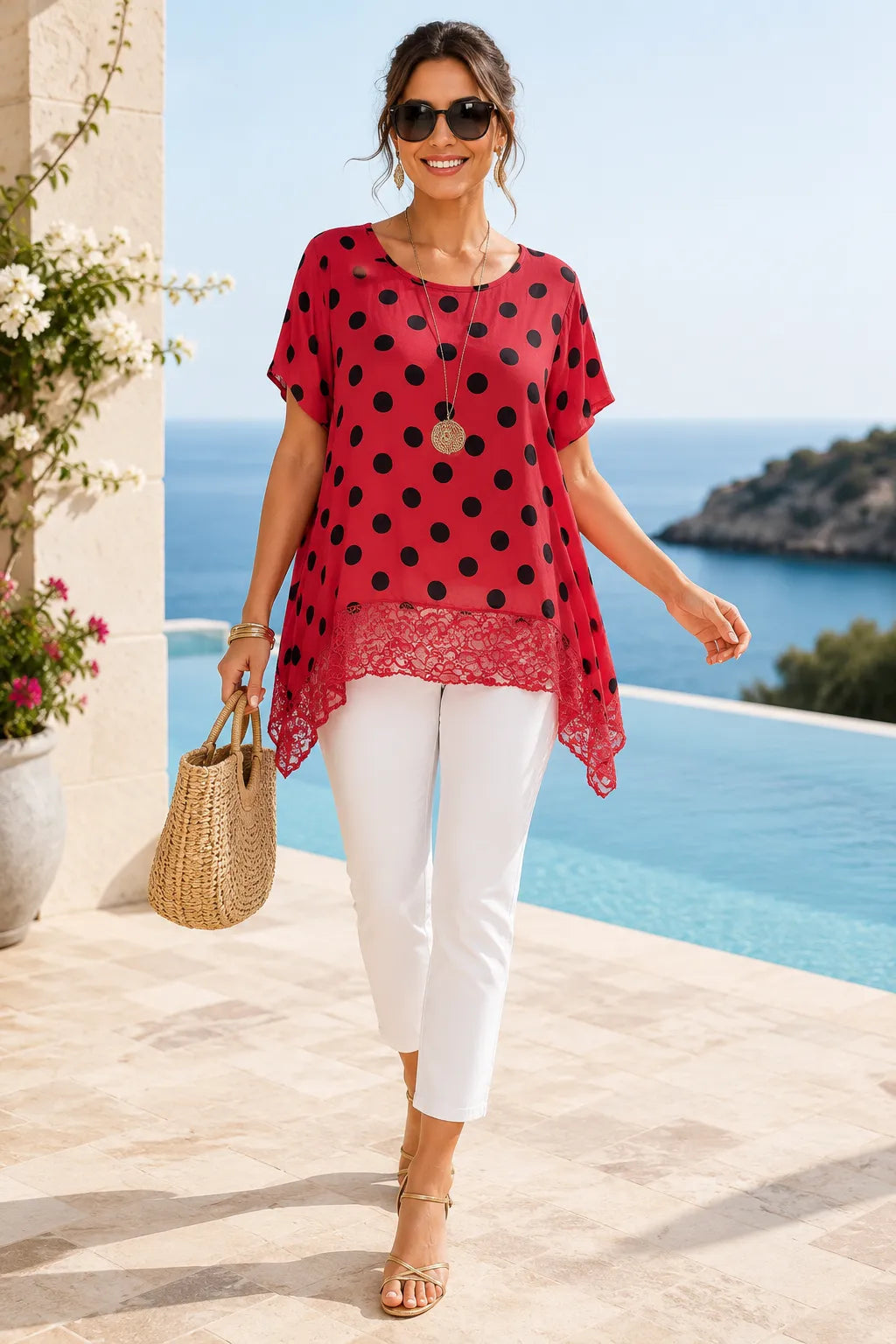 Woman in a red polka dot top and white pants walking by a pool with ocean view.