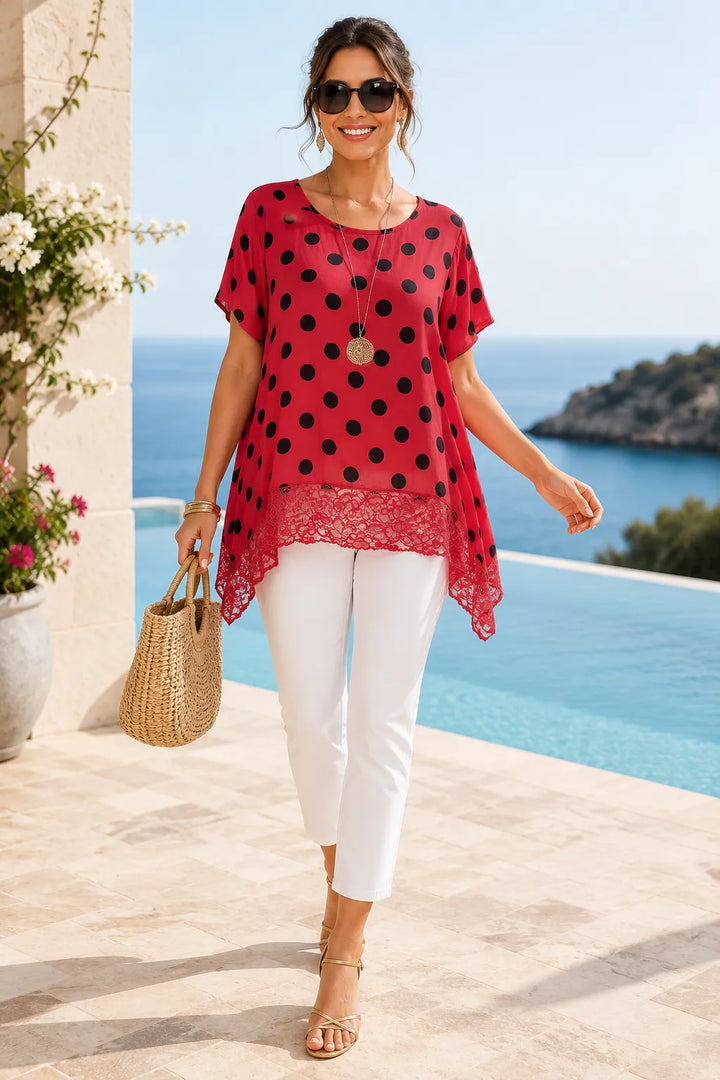 Woman in a red polka dot top and white pants walking by a pool with ocean view.