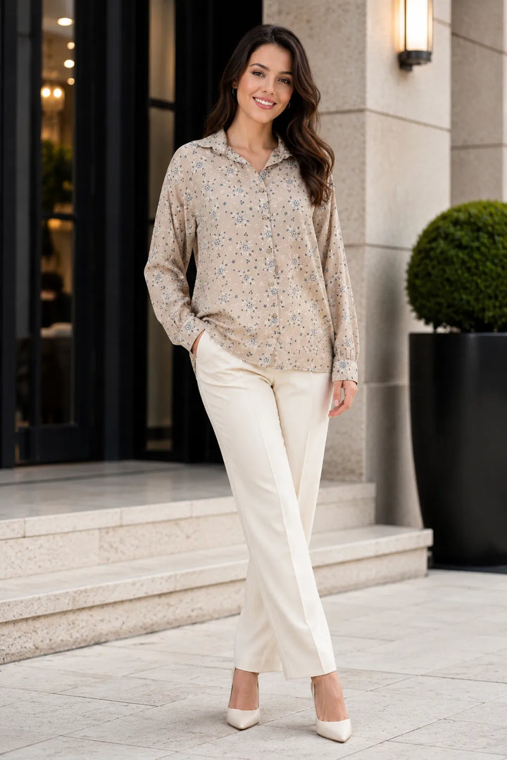Woman in a beige patterned blouse and white pants standing outside a building.