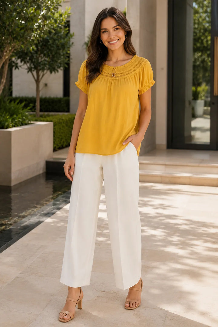 Woman wearing a yellow blouse and white pants standing outdoors.