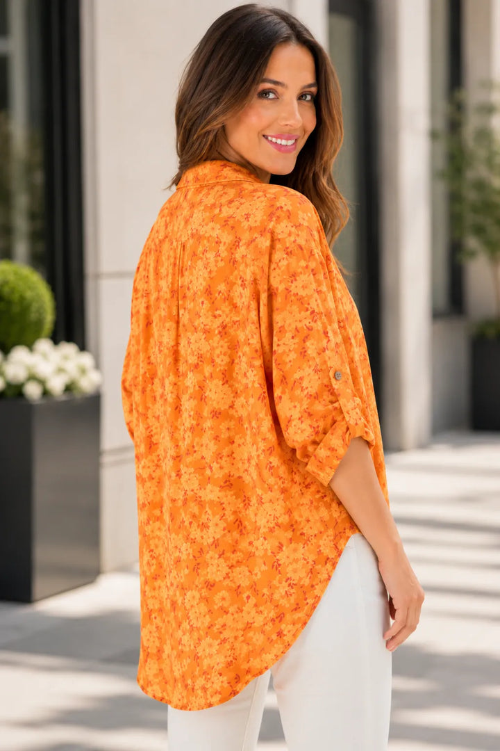 Woman wearing an orange floral blouse standing outdoors.