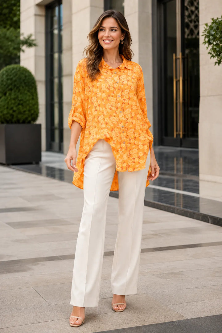 Woman wearing an orange floral blouse and white pants standing in front of a building.