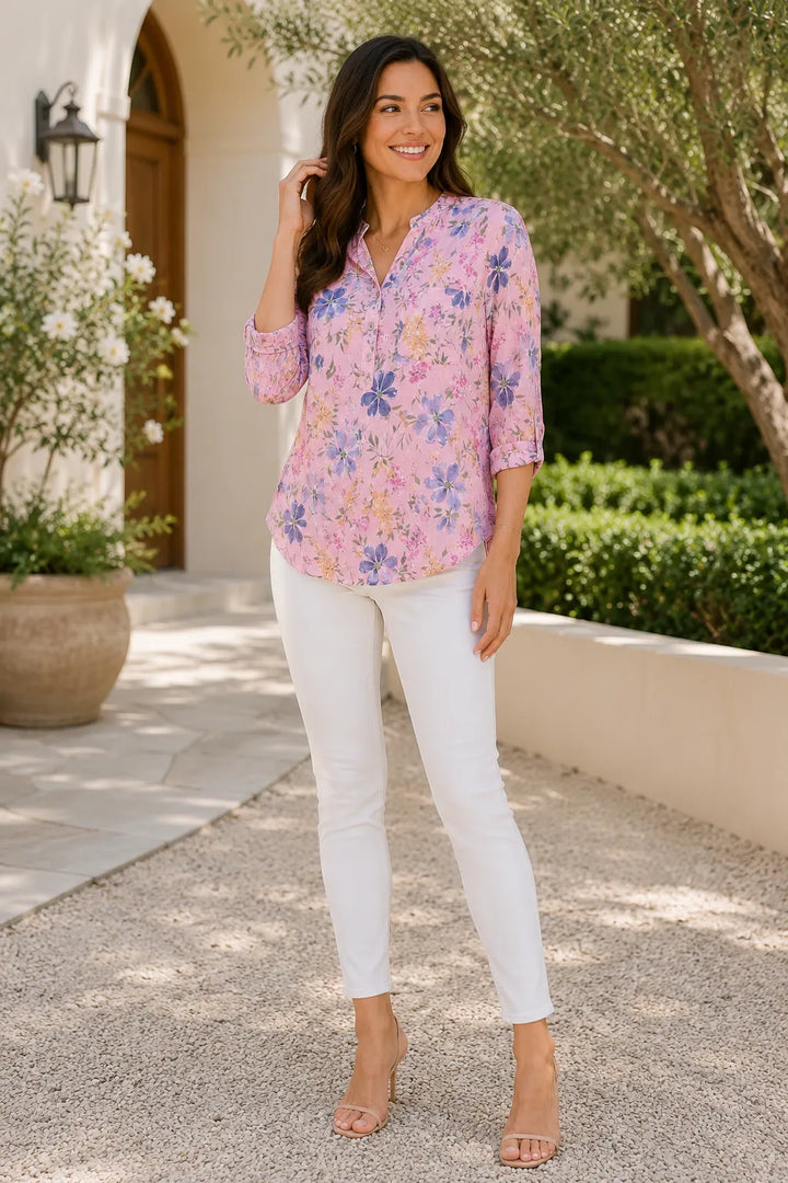 Woman wearing a pink floral blouse and white pants standing outdoors.