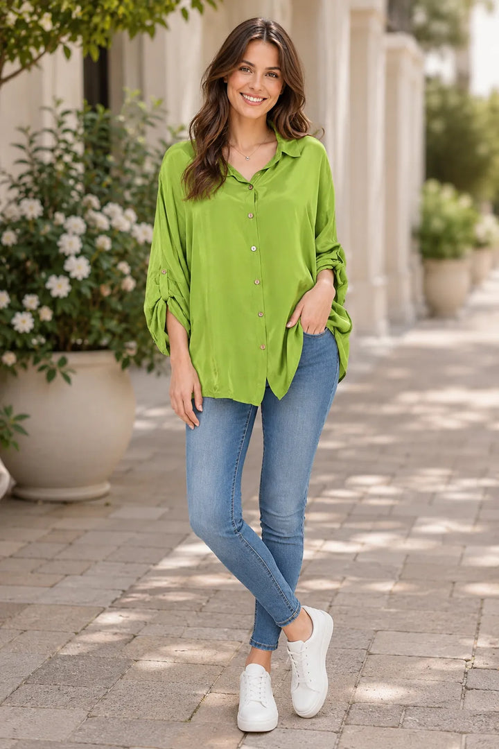 Woman wearing a green shirt and blue jeans standing on a paved walkway with plants in the background.