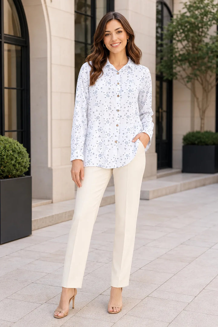 Woman wearing a white blouse with blue patterns and beige pants standing in front of a building.