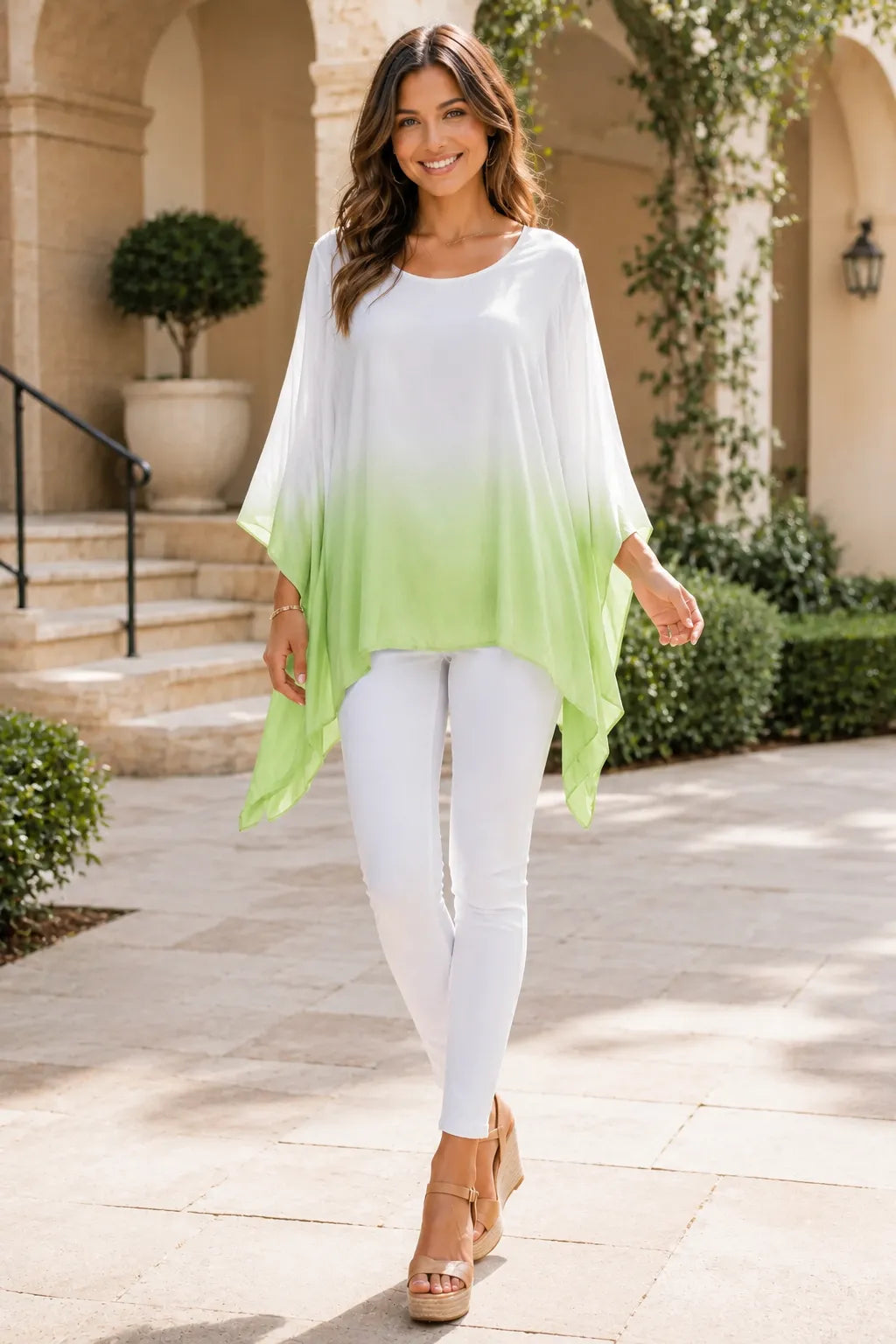 Woman wearing a white and green gradient top with white pants in an outdoor setting.