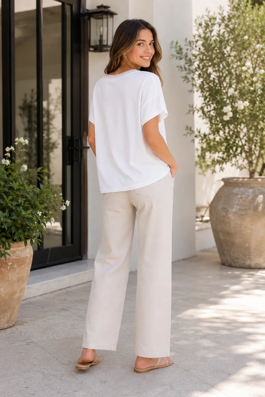 Back view of white oversized T-shirt with pink neckline trim, styled with beige wide-leg trousers and sandals