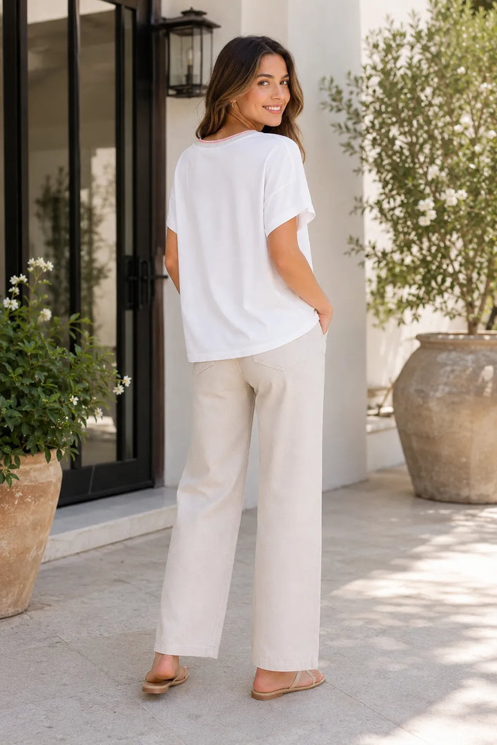 Back view of white oversized T-shirt with pink neckline trim, styled with beige wide-leg trousers and sandals