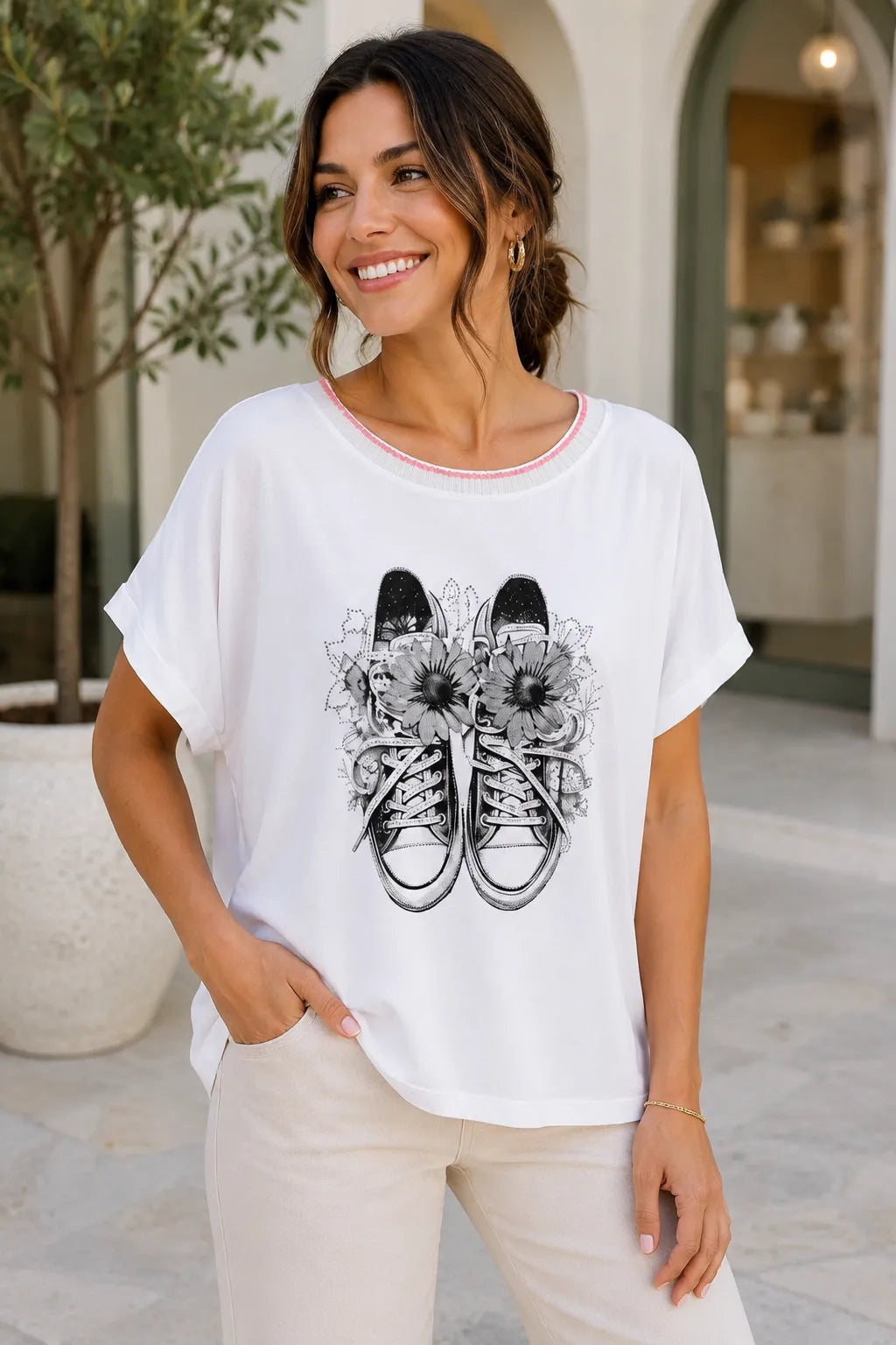 Woman wearing a white t-shirt with a graphic design of sneakers and flowers, standing outdoors.
